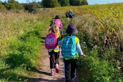 Barnehageunger med sekker på ryggen som løper gjennom en åker på en sti.